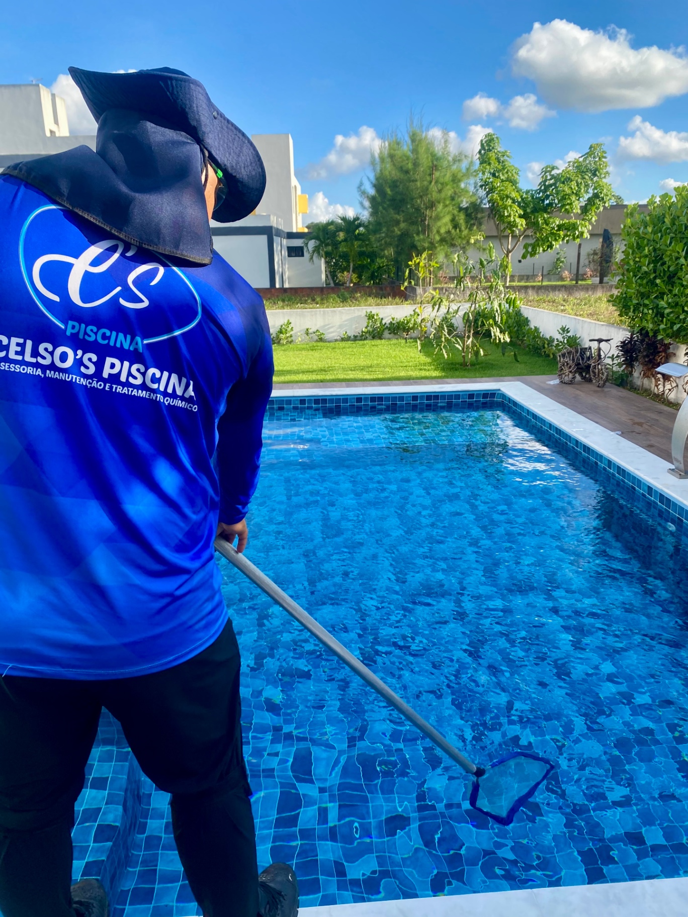 Funcionário da Celso's Piscinas de costas com a camisa da empresa visível durante limpeza da piscina